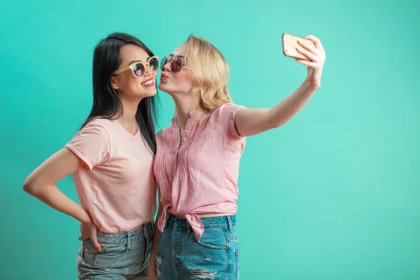 Farklı kızlar günlük kıyafetlerle çekim yapıyor. Mavi arka planda izole edilmiş selfie çekiyorlar.. — Stok fotoğraf