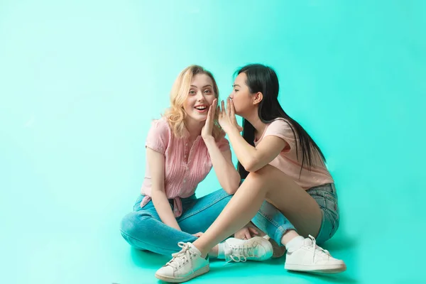 Twee multi-etnische vrouwen zitten op de vloer rug aan rug geïsoleerd op blauwe achtergrond — Stockfoto