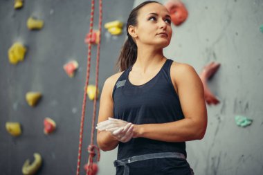 Tebeşir gibi elleri olan genç bir kadın kapalı spor salonunun duvarında poz veriyor.
