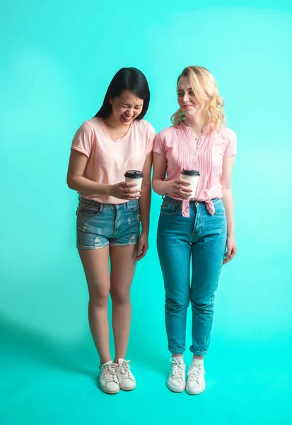 Pár mnohonárodních dívek držících odnášející kávu izolovanou přes modrou — Stock fotografie