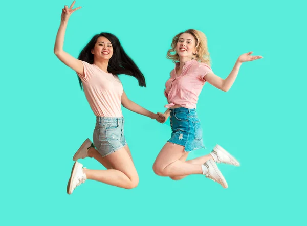 Dos mujeres jóvenes felices y despreocupadas saltando sobre fondo azul — Foto de Stock