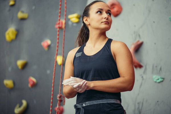 young woman with chalked hands posing at indoor climbing gym wall