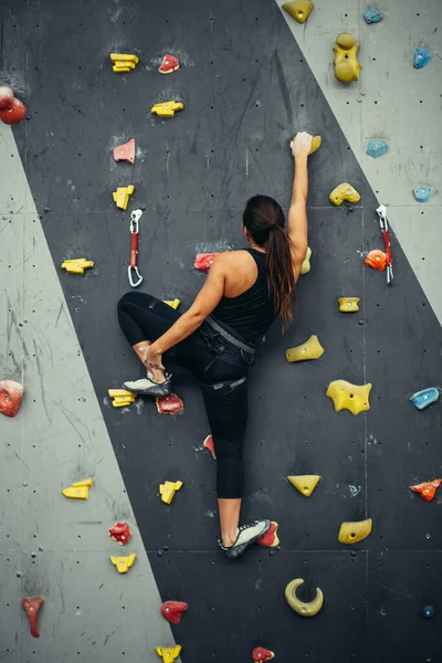 Frau übt sich im Klettern an künstlicher Wand in Innenräumen. Aktiver Lebensstil und Boulderkonzept. — Stockfoto