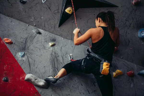 Femeia ajunge în partea de sus a peretelui artificial de bolovani în timp ce exercită în sala de sport . — Fotografie, imagine de stoc