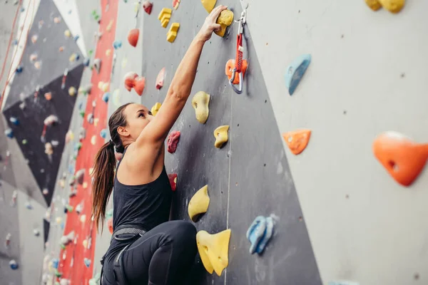 Sportovní mladá žena školení v barevné horolezectví tělocvična. — Stock fotografie