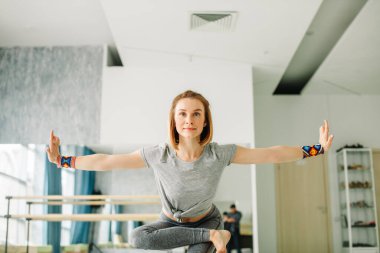 İyi aydınlatılmış spor salonunda yoga yaparken denge egzersizleri yapan bir kadın.