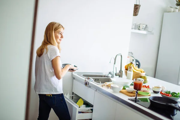 Jeune femme nettoie la vaisselle dans la cuisine — Photo