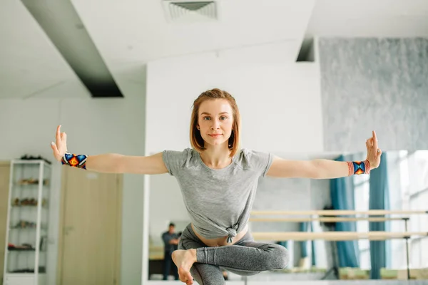 Женщина делает упражнения балансировки во время тренировки йоги в хорошо освещенном спортзале — стоковое фото