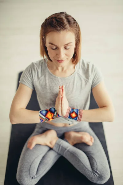 Sporty woman sitting cross-legged in lotus pose in bright room