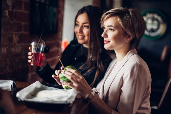 Két barátnő vacsorázik zöld szendviccsel a hamburgerbárban.. — Stock Fotó