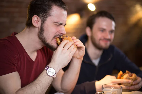 二つの幸せな男性の友人食べるおいしいハンバーガーでバー. — ストック写真