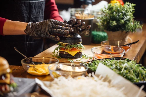 El chef prepara una hamburguesa con carne, ensalada y verduras. — Foto de Stock