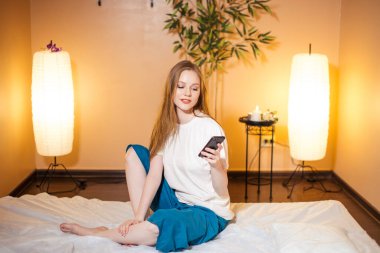 Kaplıcada masaj beklerken akıllı telefon kullanan sevimli sarışın kadın.