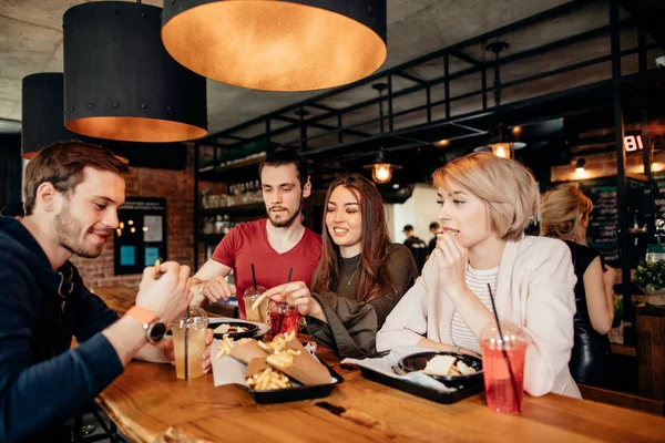 Amici che mangiano patatine fritte e hamburger insieme al ristorante all'aperto sotto il sole estivo — Foto Stock