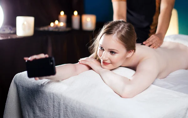 Jovem mulher bonita wtaking selfie no salão de spa ao receber de volta massagem — Fotografia de Stock
