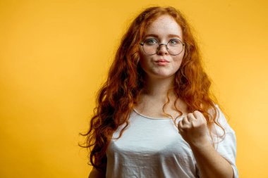 Genç ve güzel kızıl kadın sinirli ve agresif bir ifadeyle yumruğunu gösteriyor.