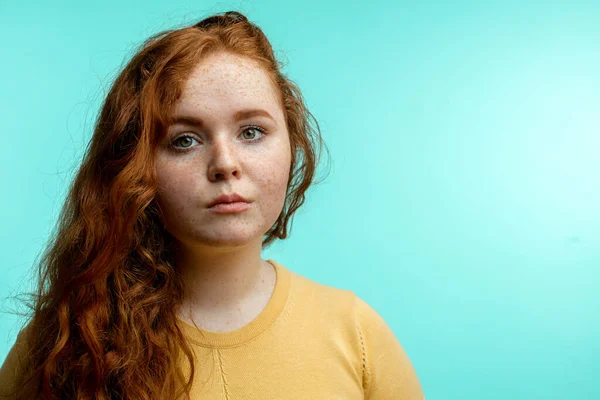 Menina ruiva com cabelo encaracolado cruzado sorrindo olhando para a câmera sobre fundo azul — Fotografia de Stock