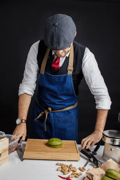 Aşçı stüdyoda, siyah duvara karşı tahta bir masanın yanında duruyor.. — Stok fotoğraf