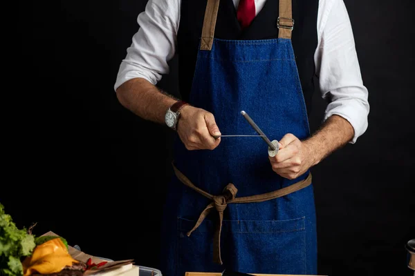 상업용 주방에서 한 남성 요리사가 칼을 날카롭게 자르고 있는 모습 — 스톡 사진