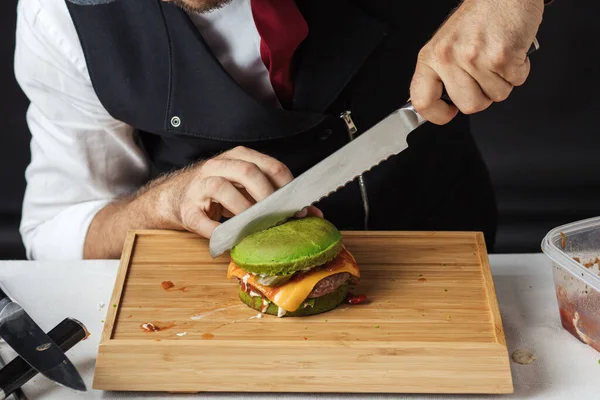 Proces jedzenia hamburgerów. Mistrz Cook cięcia smaczny hamburger z bułki szpinak — Zdjęcie stockowe