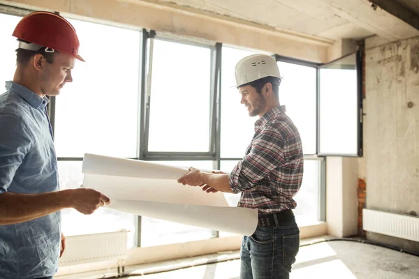 Dois construtores bonitos estão desdobrando um papel — Fotografia de Stock