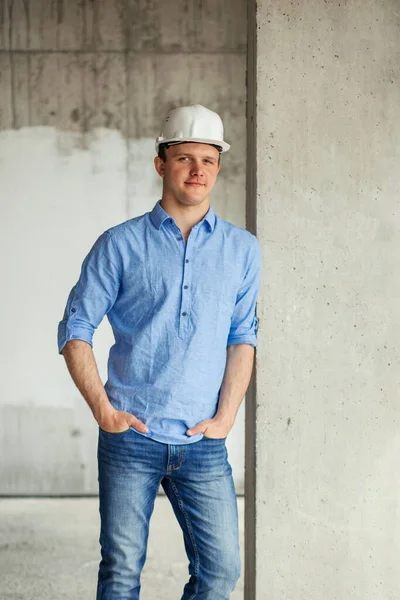 smiling architect wearing blue shirt and jeans standing near the door