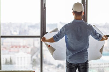 Arka plan fotoğrafını kapat. Genç inşaatçı inşaat modelini inceliyor.