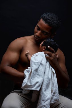Vahşi, güçlü afro adam yeni doğmuş çocuğuyla oturuyor.