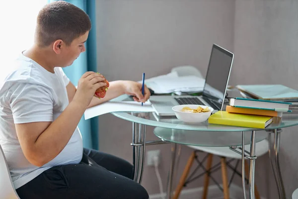 Білий підліток їсть під час домашнього завдання вдома — стокове фото