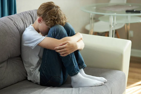 年轻的高加索少年独自坐在沙发上，脸朝下哭泣 — 图库照片