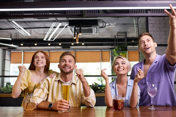 Dos parejas viendo el deporte en la televisión juntos bebiendo cerveza animando al equipo y celebrando — Foto de Stock