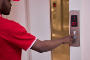 Afro siyah üniformalı bir erkek ve asansörün yanında teslimat emirleri var.
