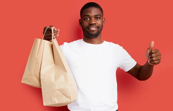 Junger afrikanischer Kurier hält Papiertüten mit Lebensmitteln in der Hand — Stockfoto