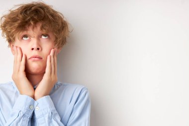 Şaşkın kıvırcık beyaz çocuk yanakları tutuyor ve düşünüyor