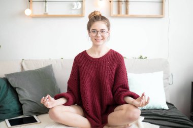 Çekici fit kız kanepede yoga pozisyonunda oturuyor.