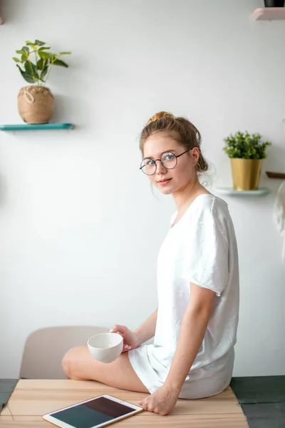 Uma menina bonita em roupas casuais sentado sobre a mesa na moderna sala de cozinha — Fotografia de Stock