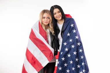 Omuzlarında Amerikan bayrağı olan güzel, gülümseyen kadınlar kameraya bakıyor.