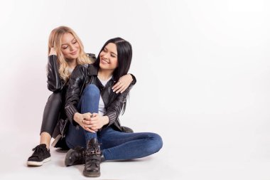 İki mutlu ve sevecen genç bayan yerde oturup eğleniyorlar.