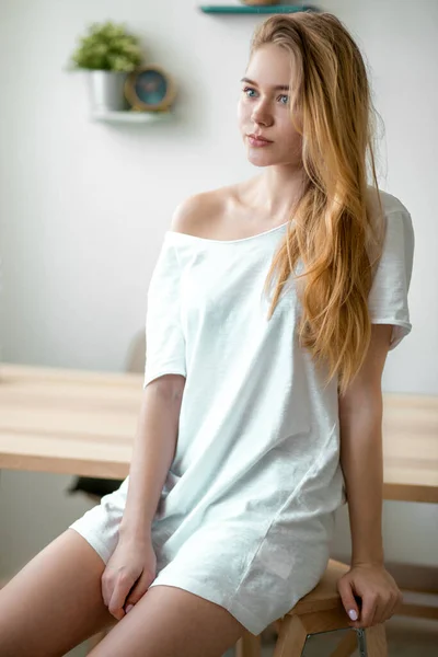 A young beautiful woman in white dress sitting on a chair at home — Stock Photo, Image