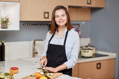 Neşeli iyimser kız salatalık keserken kameraya bakıyor.