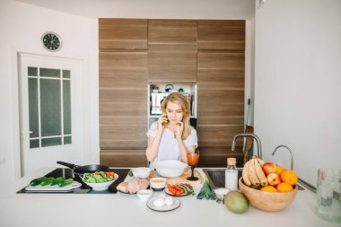 . Genç ve güzel bir kadın yemek pişirirken telefonla konuşuyor.