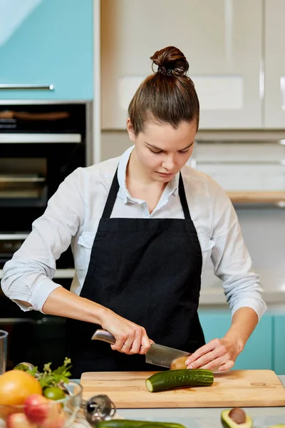 Ung vacker kvinna skära kiwi i köket med modern inredning — Stockfoto