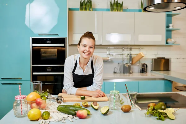 Örömteli nő fekete kötényben pózol a kamerának a konyhában — Stock Fotó