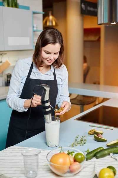 Eine Hausfrau, die Kiwi hält und sie in den Cocktail gibt — Stockfoto