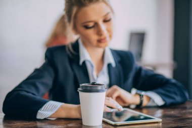 Sarışın kızın önünde plastik bir bardak kahve var. Bulanık arkaplan