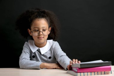 Gözlüklü akıllı küçük kız okumak için bir kitap seçiyor.