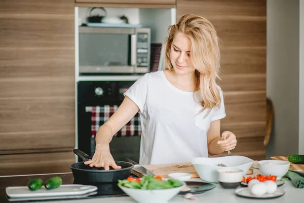 Young blond girl checking the frying pan. — Stock Photo, Image