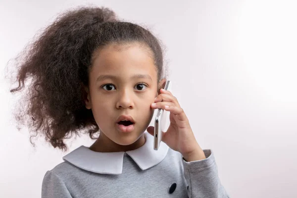 Förvånad vacker flicka med fluffigt långt svart hår stående med mobiltelefon — Stockfoto