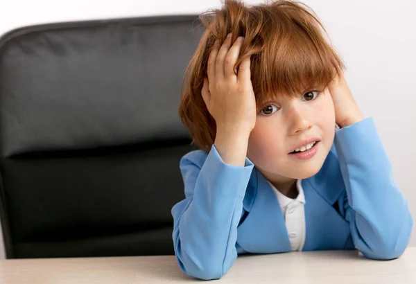 Niño pelirrojo tocándose la cabeza mientras está sentado en la mesa — Foto de Stock