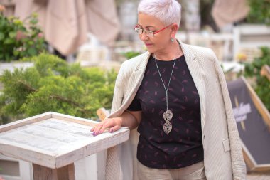 Düşünceli, güzel, yaşlı bir kadın tatil köyünde geziniyor.